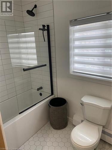 Bathroom featuring a baseboard heating unit, bath / shower combo with glass door, tile patterned floors, and toilet - 67 Louisa Street, Kitchener, ON - Indoor Photo Showing Bathroom