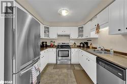 Kitchen featuring appliances with stainless steel finishes, sink, white cabinets, and a textured ceiling - 