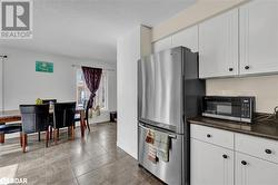 Kitchen with white cabinetry, stainless steel fridge, a textured ceiling, and light tile patterned flooring - 