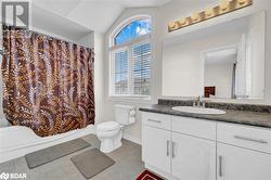 Full bathroom with vaulted ceiling, tile patterned flooring, vanity, toilet, and shower / bath combo with shower curtain - 