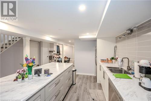 Kitchen featuring dishwasher, sink, decorative backsplash, light stone counters, and light wood-type flooring - 82 Conway Drive, Kitchener, ON - Indoor Photo Showing Kitchen With Double Sink