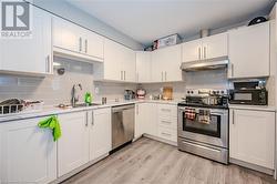 Kitchen with sink, stainless steel appliances, light hardwood / wood-style floors, decorative backsplash, and white cabinets - 