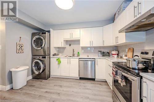 Kitchen featuring sink, white cabinetry, stainless steel appliances, stacked washer and clothes dryer, and tasteful backsplash - 82 Conway Drive, Kitchener, ON - Indoor