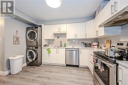 Kitchen featuring sink, white cabinetry, stainless steel appliances, stacked washer and clothes dryer, and tasteful backsplash - 