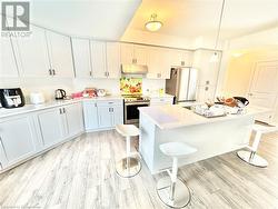 Kitchen with hanging light fixtures, stainless steel appliances, a kitchen breakfast bar, and light wood-type flooring - 