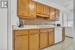 Kitchen with light tile patterned floors, dishwasher, backsplash, and sink - 