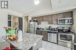 Kitchen featuring light stone counters, a center island, stainless steel appliances, a sink, and dark brown cabinetry - 