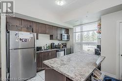 Kitchen with stainless steel appliances, light tile patterned flooring, a peninsula, and dark brown cabinets - 