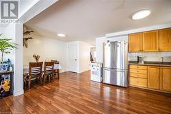 Kitchen featuring dark wood-style flooring, dark countertops, decorative backsplash, brown cabinetry, and freestanding refrigerator - 