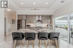 Kitchen featuring wall chimney range hood, high end appliances, gray cabinets, and a breakfast bar - 