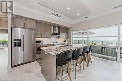 Kitchen with crown molding, appliances with stainless steel finishes, a kitchen island with sink, light stone countertops, and wall chimney exhaust hood - 