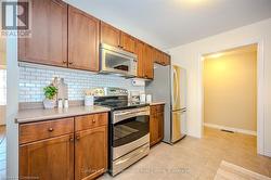 Kitchen with brown cabinets, light tile patterned floors, stainless steel appliances, light countertops, and decorative backsplash - 