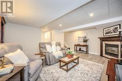 Living area with stairway, light wood-style flooring, a glass covered fireplace, a drop ceiling, and baseboards - 