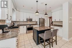 Kitchen featuring stainless steel appliances, dark countertops, a sink, and light tile patterned floors - 