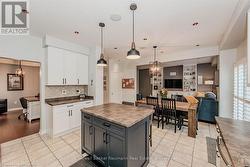 Kitchen with white cabinetry, open floor plan, backsplash, dark countertops, and decorative light fixtures - 