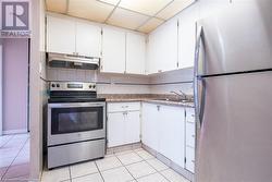 Kitchen with appliances with stainless steel finishes, a drop ceiling, white cabinetry, and under cabinet range hood - 