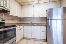 Kitchen with light tile patterned floors, under cabinet range hood, a sink, appliances with stainless steel finishes, and decorative backsplash - 