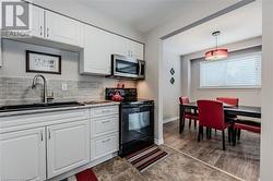 Kitchen with sink, white cabinetry, decorative light fixtures, black range with electric cooktop, and decorative backsplash - 