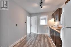 Kitchen with decorative backsplash, light wood-style floors, dark brown cabinets, white appliances, and baseboards - 