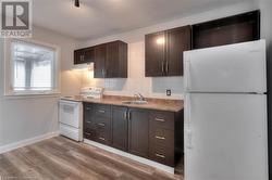 Kitchen featuring white appliances, tasteful backsplash, wood finished floors, under cabinet range hood, and a sink - 