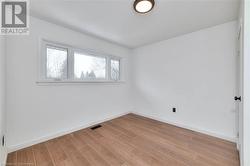 Empty room with light wood finished floors, visible vents, and baseboards - 