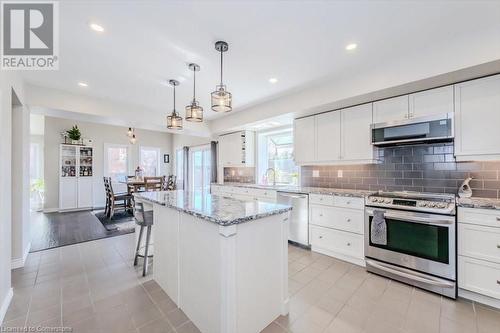 Kitchen with light stone counters, stainless steel appliances, white cabinetry, decorative light fixtures, and backsplash - 598 Coppercroft Court, Waterloo, ON - Indoor Photo Showing Kitchen With Upgraded Kitchen