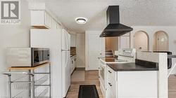 Kitchen with dark countertops, white appliances, wood finished floors, and exhaust hood - 