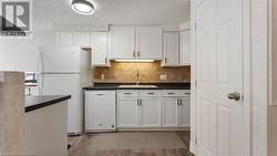 Kitchen featuring white appliances, wood finished floors, a sink, backsplash, and dark countertops - 