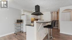 Kitchen featuring dark wood finished floors, dark countertops, freestanding refrigerator, island exhaust hood, and white cabinetry - 