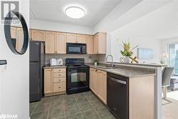 Kitchen with a sink, a peninsula, black appliances, and light brown cabinetry - 