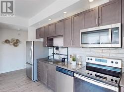 Kitchen featuring dark brown cabinetry, light wood finished floors, tasteful backsplash, appliances with stainless steel finishes, and a sink - 