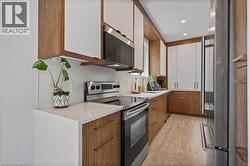 Kitchen featuring appliances with stainless steel finishes, decorative backsplash, light wood-style floors, brown cabinets, and light stone countertops - 