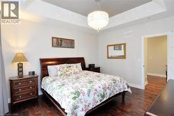 Bedroom featuring a raised ceiling, dark wood-style flooring, and a chandelier - 