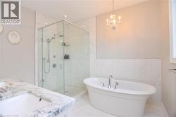 Bathroom with a freestanding tub, double vanity, a stall shower, light marble finish floors, and tile walls - 