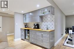 Indoor wet bar featuring gray cabinetry, glass insert cabinets, wood counters, tasteful backsplash, and light wood-style flooring - 