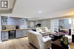 Living area featuring beverage cooler, a bar, light wood-type flooring, and recessed lighting - 