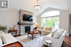 Living area featuring vaulted ceiling, dark wood-style flooring, a stone fireplace, and recessed lighting - 