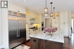 Kitchen with stainless steel appliances, glass insert cabinets, light stone countertops, backsplash, and a kitchen island with sink - 