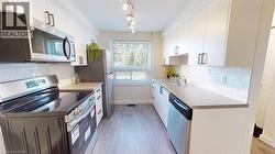 Kitchen with stainless steel appliances, tasteful backsplash, light wood-style flooring, and white cabinetry - 