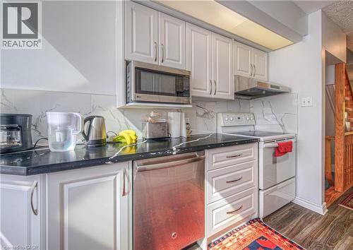 Kitchen with appliances, decorative backsplash, under cabinet range hood, white cabinetry, and dark wood finished floors - 310 Christopher Drive Unit# 15, Cambridge, ON - Indoor Photo Showing Kitchen