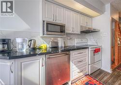 Kitchen with appliances, decorative backsplash, under cabinet range hood, white cabinetry, and dark wood finished floors - 