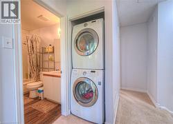 Laundry area featuring stacked washing machine and dryer, light colored carpet, and a textured ceiling - 