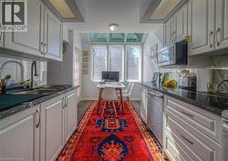 Kitchen featuring dark wood-type flooring, dark stone countertops, appliances, white cabinets - 