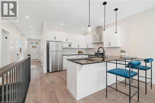 Kitchen featuring a peninsula, white cabinetry, stainless steel appliances, light wood finished floors, and wall chimney exhaust hood - 12 Washington Street Unit# 102, Norwich, ON - Indoor Photo Showing Kitchen With Upgraded Kitchen