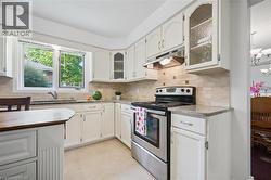 Kitchen featuring glass insert cabinets, electric stove, backsplash, under cabinet range hood, and white cabinets - 