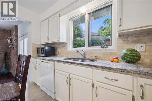 Kitchen featuring white dishwasher, stainless steel microwave, white cabinetry, backsplash, and light stone counters - 599 Beechwood Drive, Waterloo, ON - Indoor Photo Showing Kitchen With Double Sink