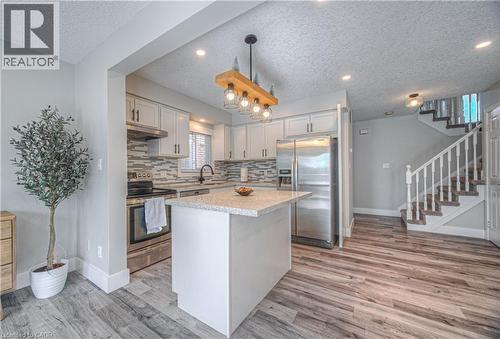 Kitchen with appliances with stainless steel finishes, decorative backsplash, a textured ceiling, decorative light fixtures, and light wood-style floors - 220 Sienna Crescent, Kitchener, ON - Indoor Photo Showing Kitchen With Stainless Steel Kitchen With Upgraded Kitchen