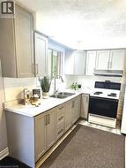 Kitchen featuring gray cabinetry, light countertops, white range with electric stovetop, a textured ceiling, and tasteful backsplash - 