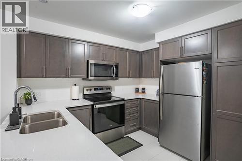 Kitchen with stainless steel appliances, decorative backsplash, light tile patterned flooring, dark brown cabinets, and light stone countertops - 85 Mullin Drive Unit# 20B, Guelph, ON - Indoor Photo Showing Kitchen With Double Sink