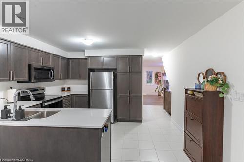 Kitchen featuring appliances with stainless steel finishes, dark brown cabinetry, a peninsula, light tile patterned flooring, and light stone countertops - 85 Mullin Drive Unit# 20B, Guelph, ON - Indoor Photo Showing Kitchen With Double Sink